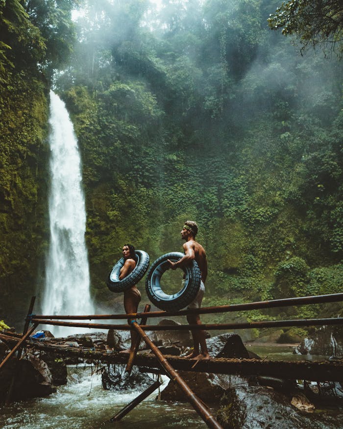 our-story A couple in swimwear with float tubes exploring a lush waterfall in Bali, Indonesia.